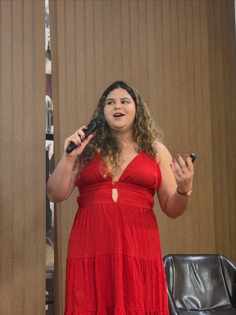 Rebeca Sousa no palco do MMMT 2026, com microfone e clicker durante a palestra.